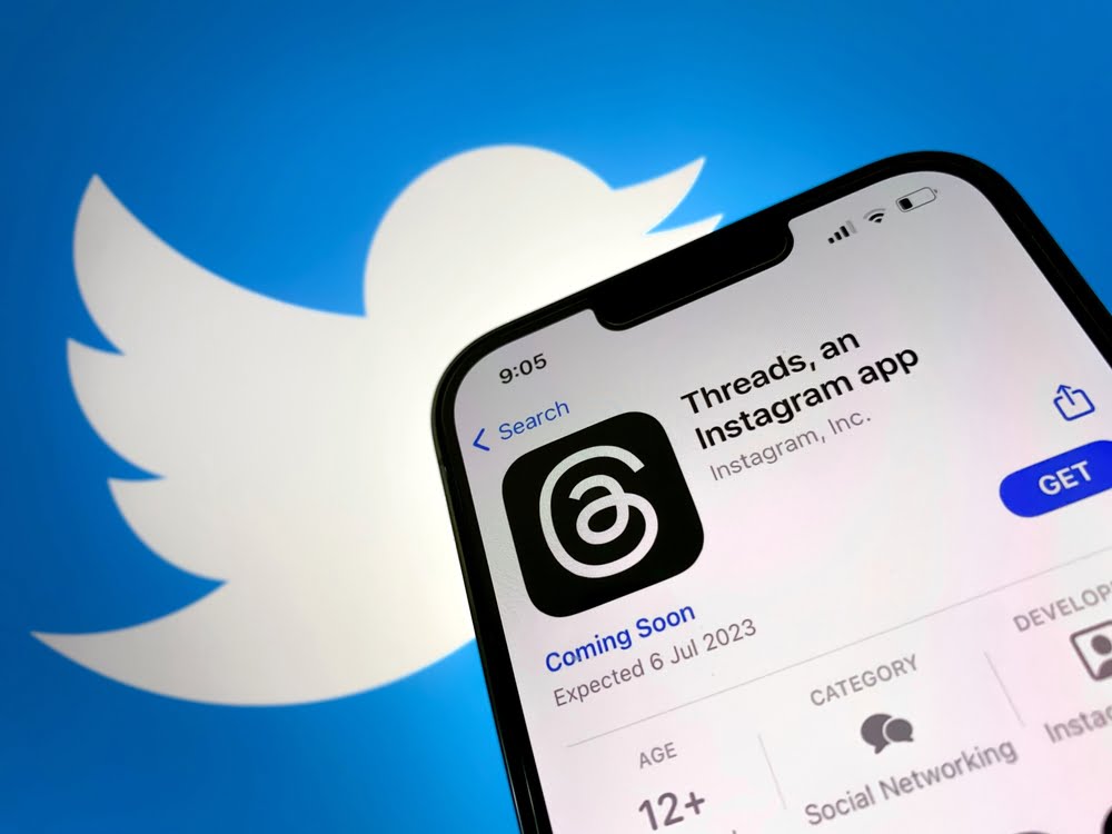 Meta Threads App on Phone, with Twitter logo in background. Twitter vs. Threads Rivalry