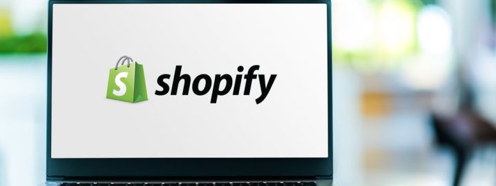 Poznan,,Pol,-,Feb,6,,2021:,Laptop,Computer,Displaying,Logo Laptop displaying the Shopify logo on its screen. The logo consists of a green shopping bag with a white 'S' on it, followed by the word 'shopify' in black text. The background of the image is blurred, suggesting an indoor setting.