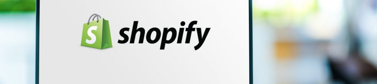 Poznan,,Pol,-,Feb,6,,2021:,Laptop,Computer,Displaying,Logo Laptop displaying the Shopify logo on its screen. The logo consists of a green shopping bag with a white 'S' on it, followed by the word 'shopify' in black text. The background of the image is blurred, suggesting an indoor setting.